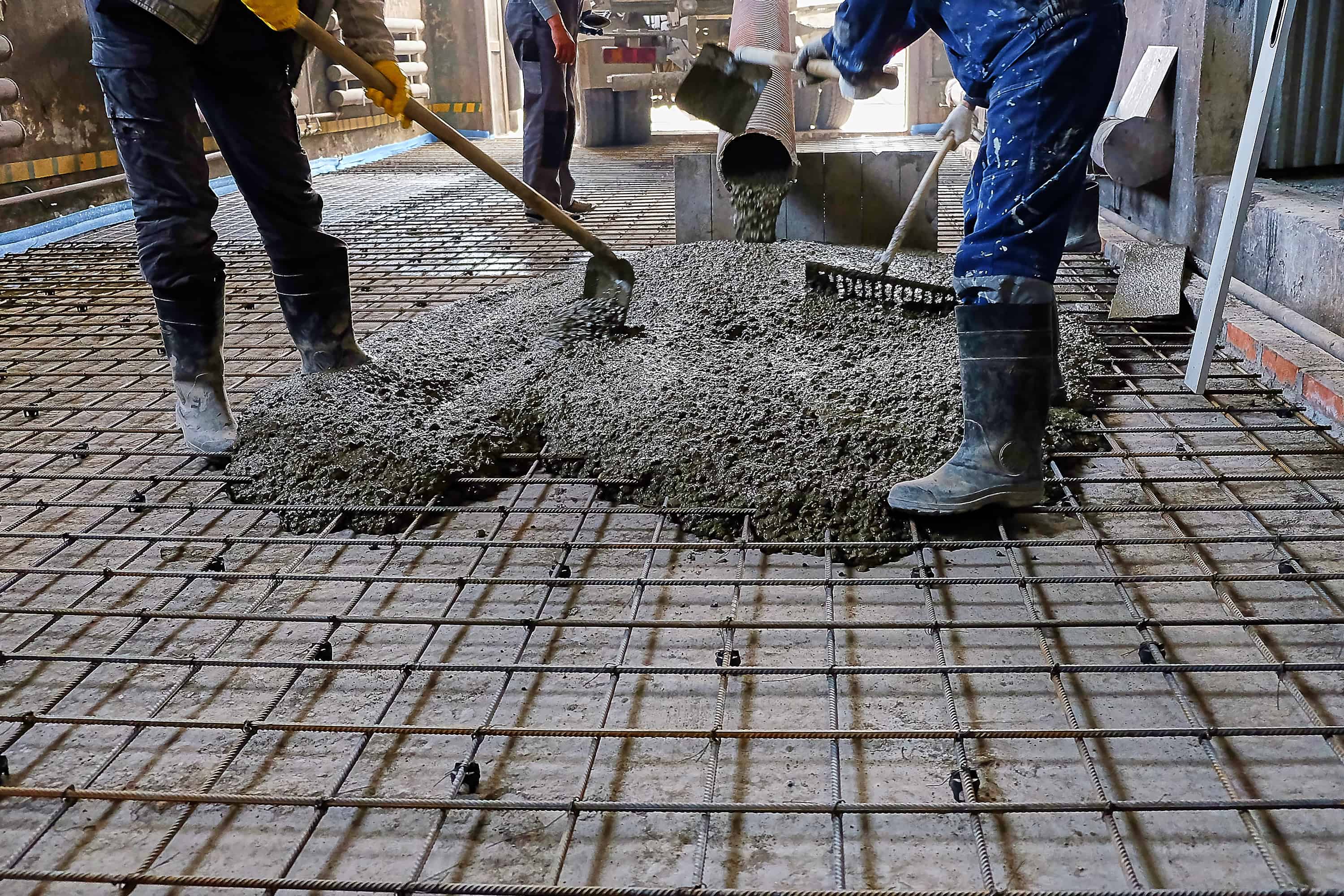 Crew spreading and levelling freshly poured concrete over steel reinforcing mesh