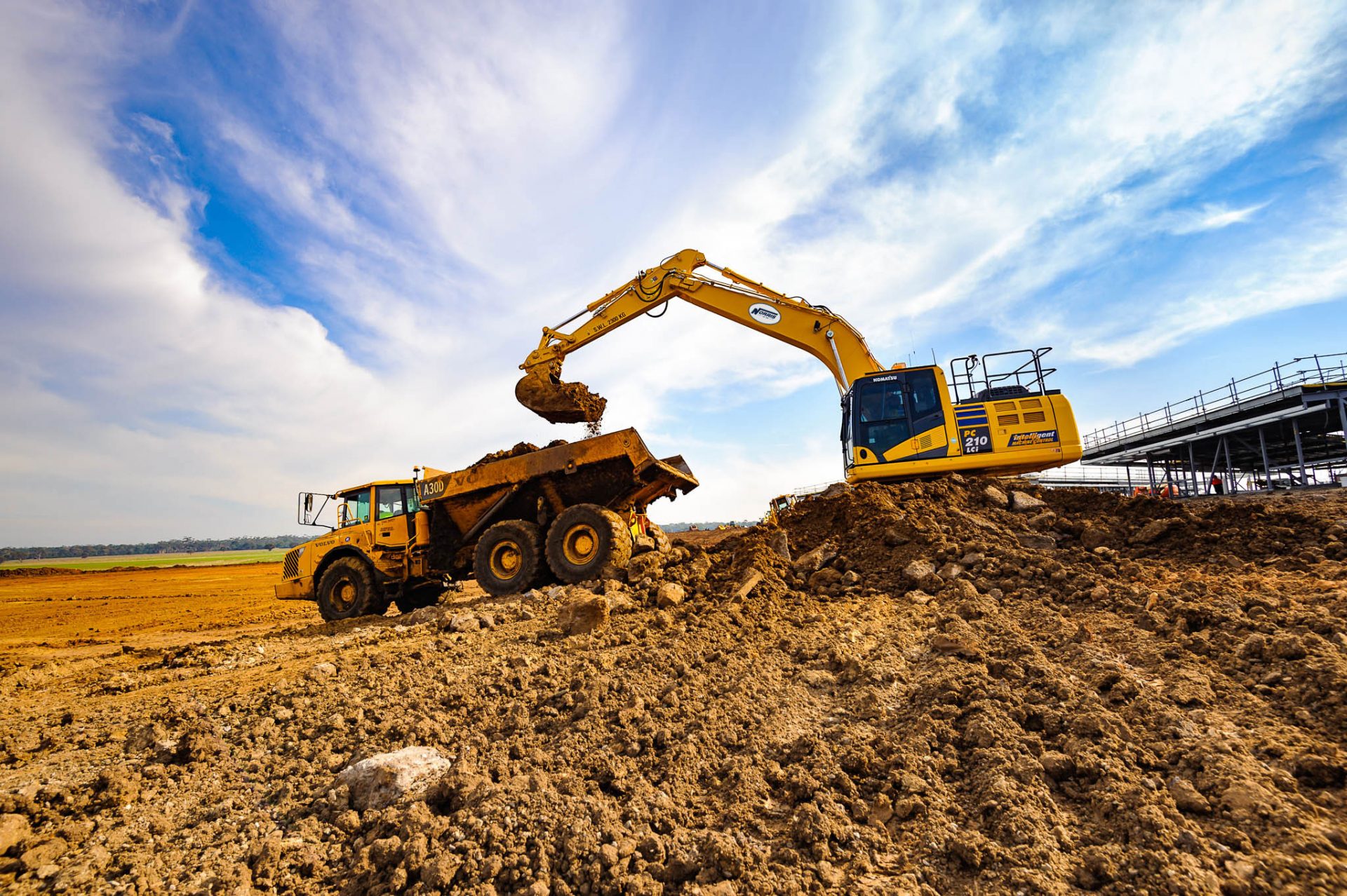 Excavator loading cut material into an articulated dump truck during bulk earthworks